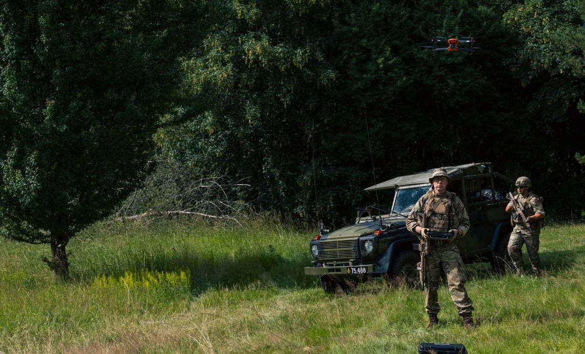 To hærhjemmeværnssoldater står i skoven med en drone og en GD i baggrunden