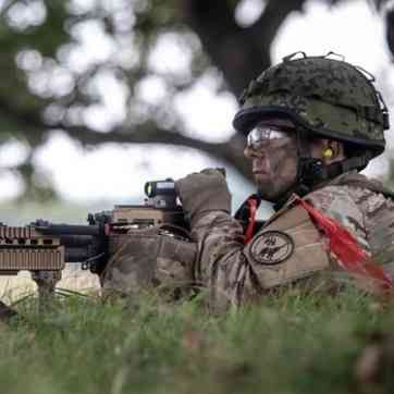Hjemmeværnssoldat ligger i højt græs med et maskingevær